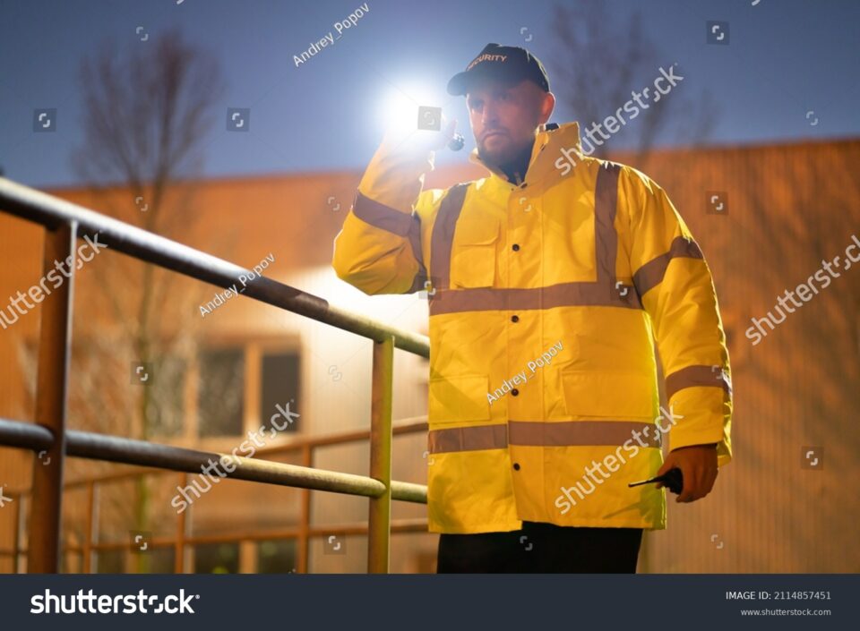 stock photo security guard walking building perimeter with flashlight at night 2114857451